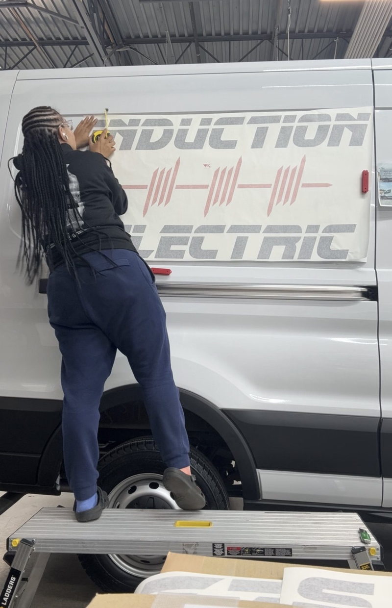 CeCe measuring and applying vinyl lettering to a white Induction Electric work van